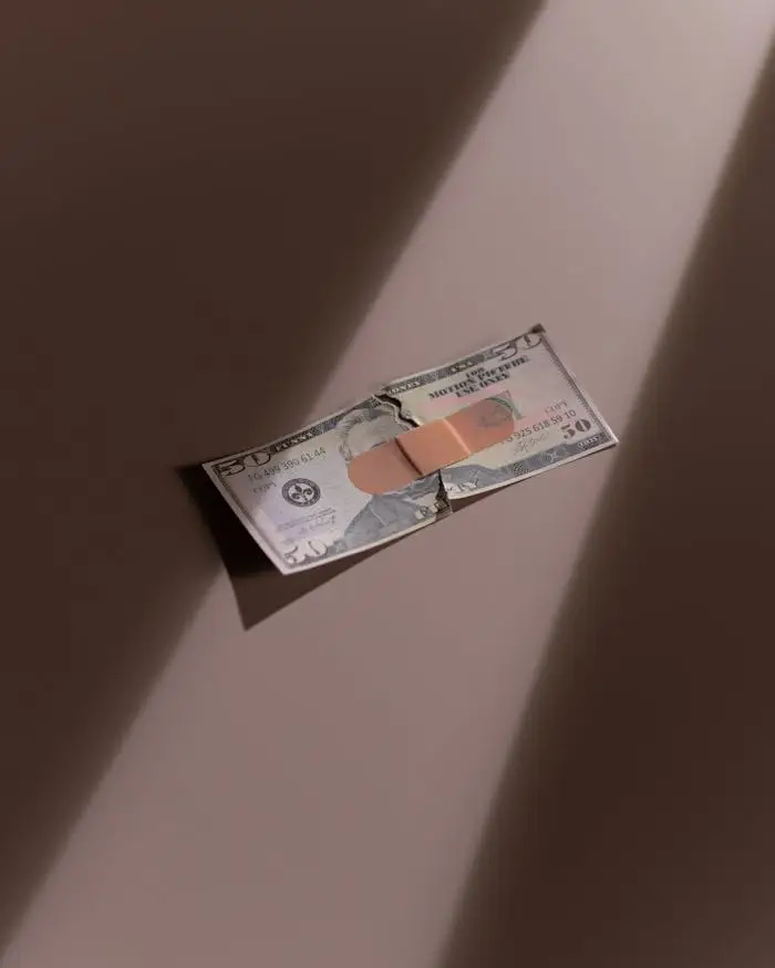 A torn dollar bill patched with a bandage, symbolizing financial recovery.